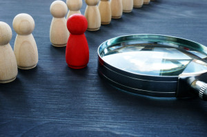 Red figurine standing next to many beige figurines and a magnifier. Representing a targeted form a lead retrieval.